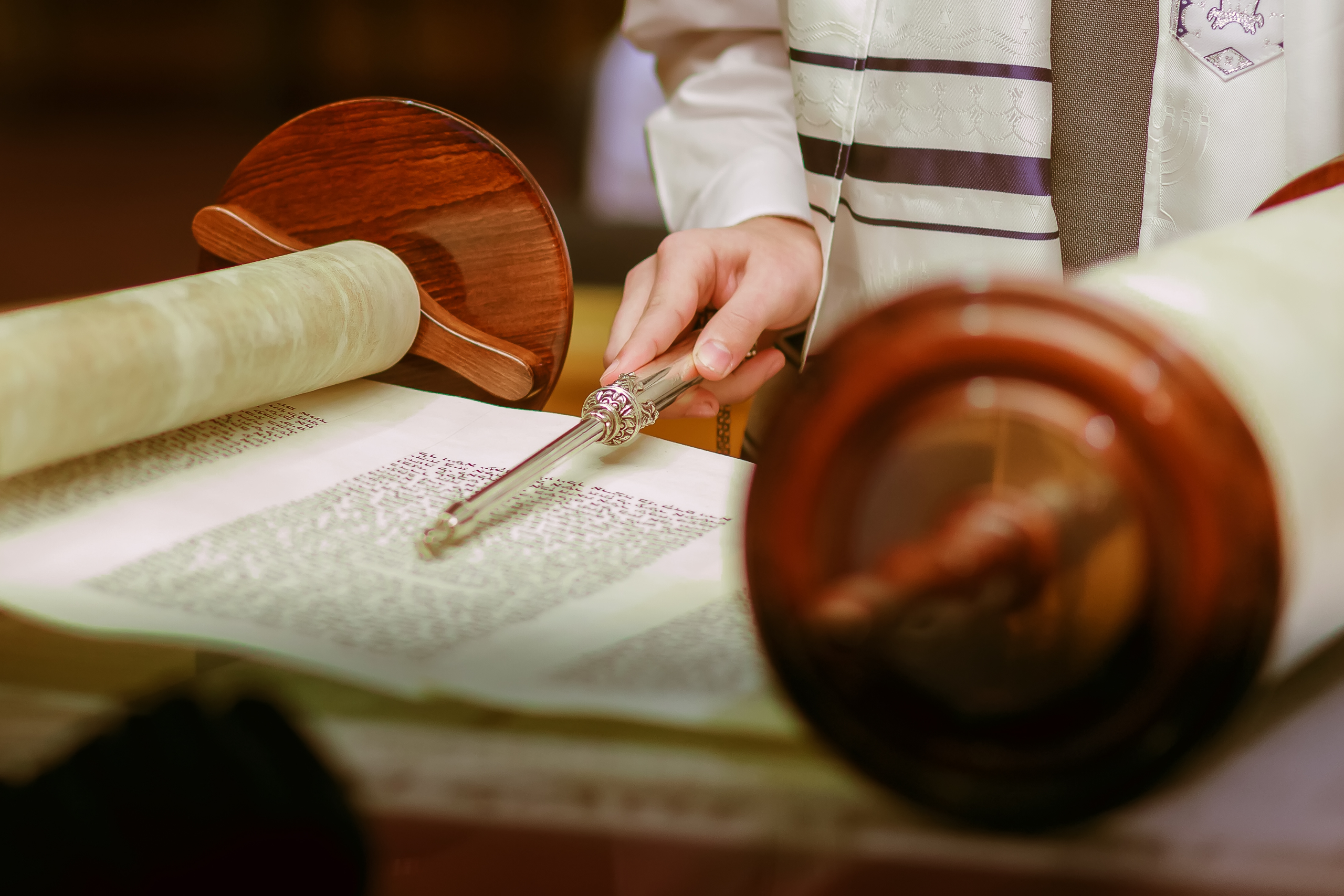 Image of an open Torah scroll with a person holding a yad to the text
